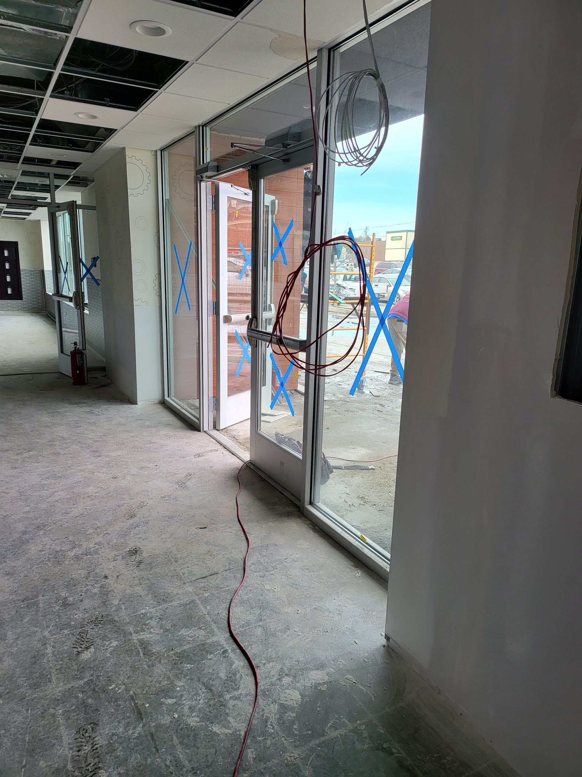 Construction hallway with open glass doors, electrical wiring, and blue xs.