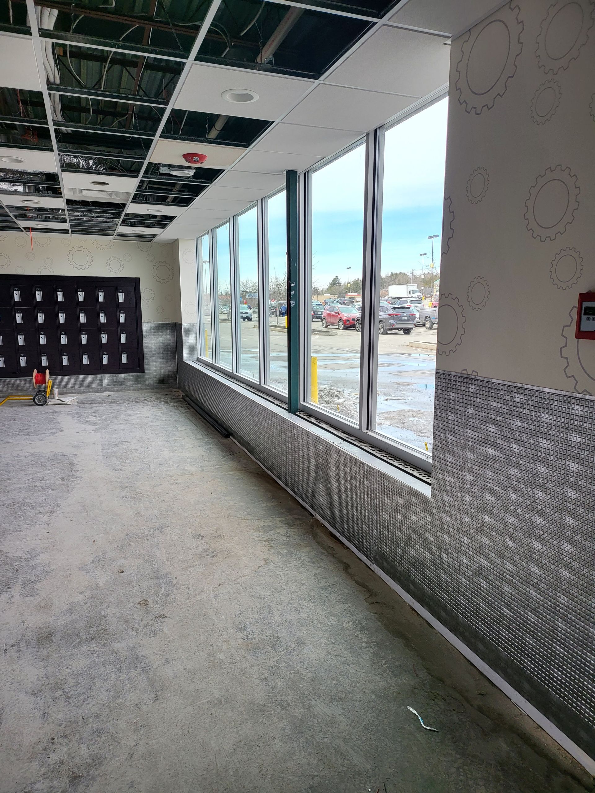 Interior of a commercial space under construction with large windows overlooking a parking lot.