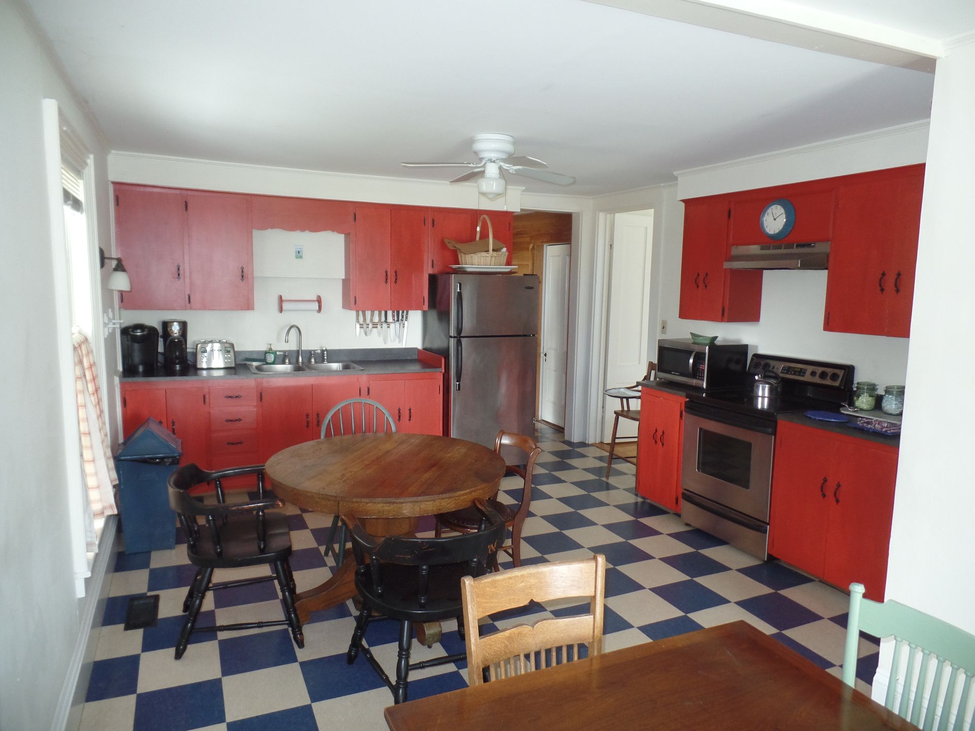 Red kitchen cabinets and blue and white checkered floor, with a wooden table and chairs in the dining area.