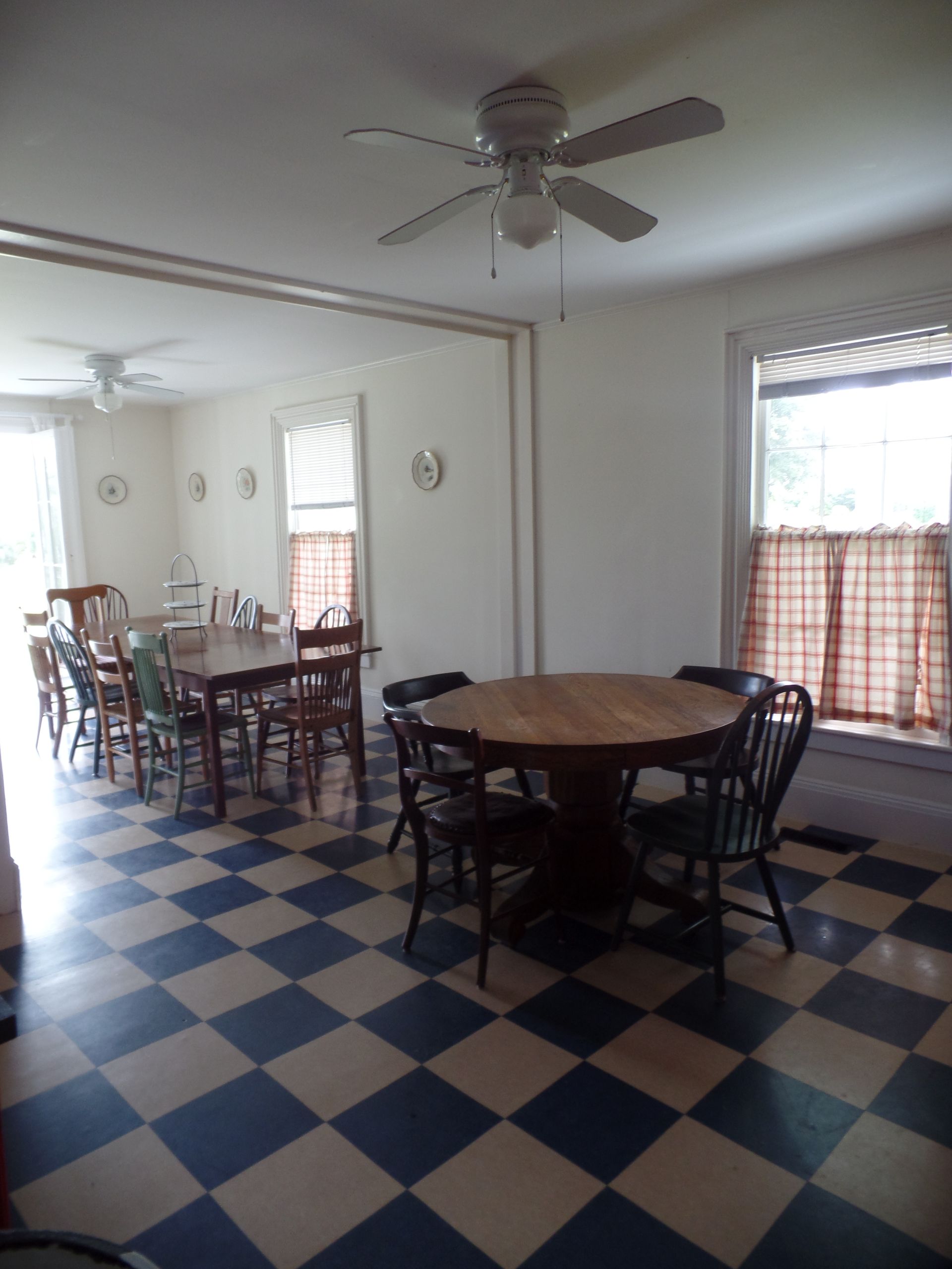 Dining room with checkered blue and white floor, two tables, chairs, and two ceiling fans.