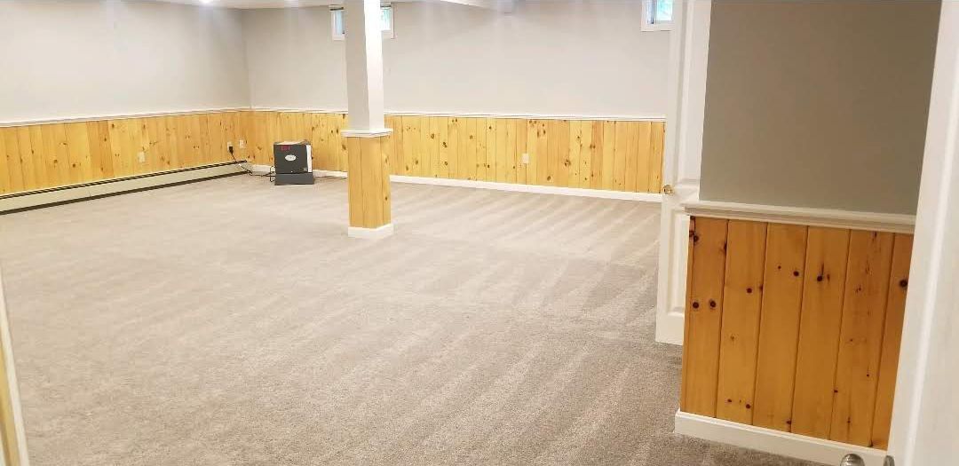 Empty basement room with wood paneling and gray carpet.