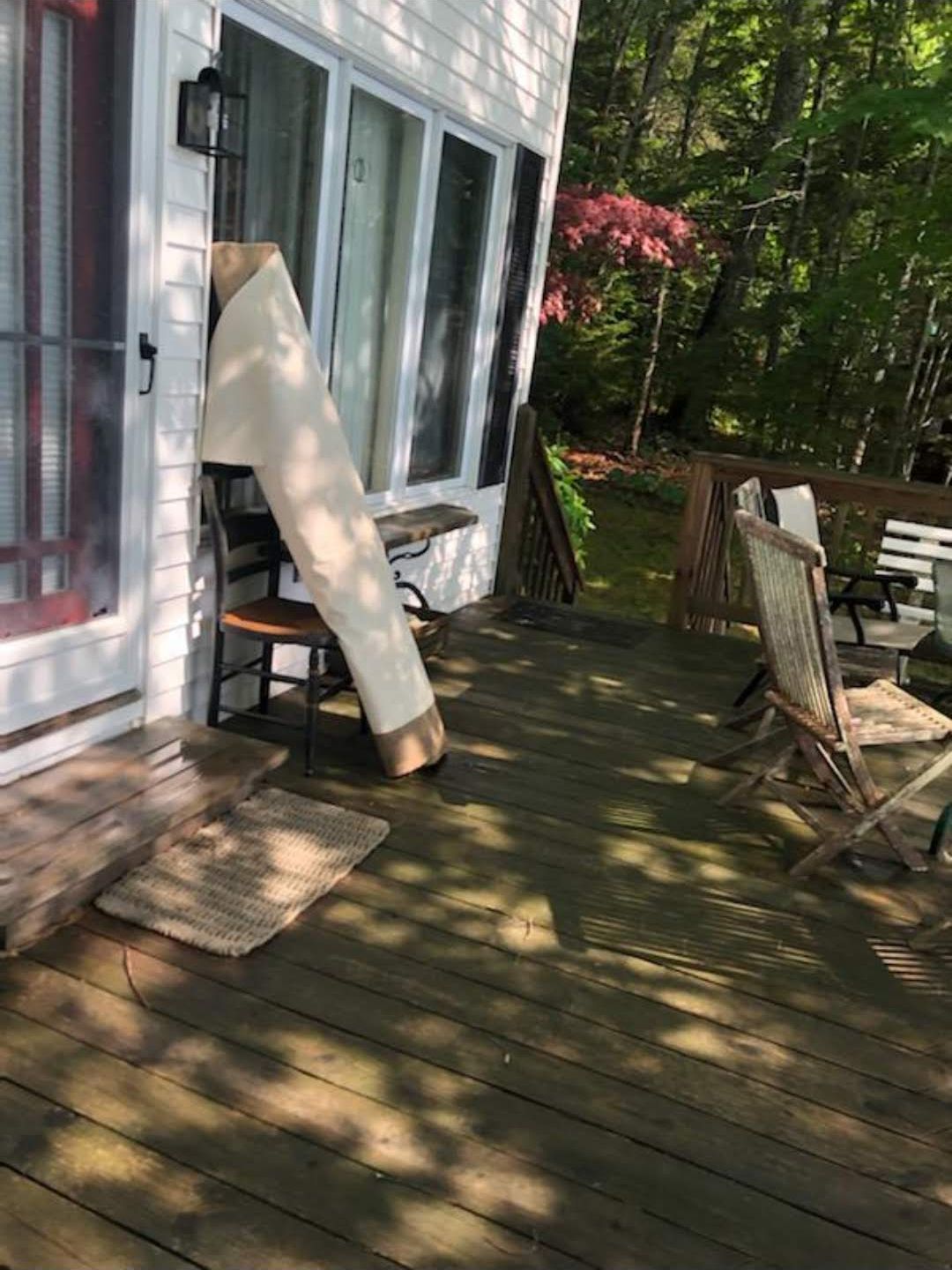 Wooden deck with chairs, house with windows, and a long, rolled-up tan object leaning against it.
