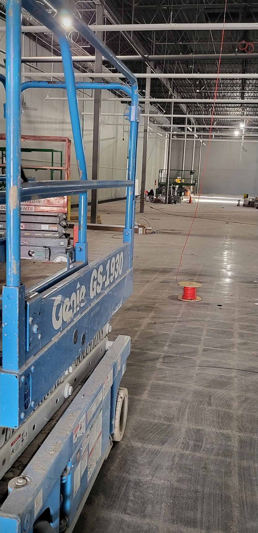 Blue scissor lift inside a construction site, with a concrete floor and exposed ceiling.