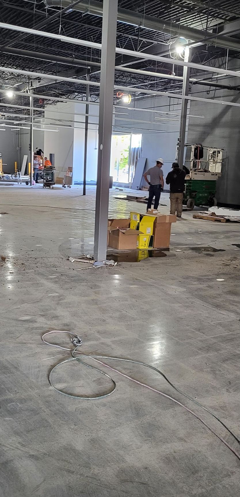 Construction site interior, concrete floor, workers, exposed ceiling, boxes, and wires.