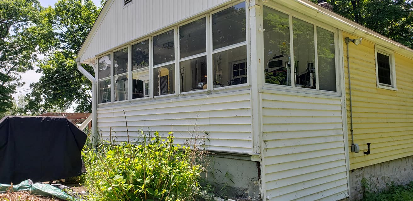 A yellow house with a screened in porch and lots of windows.