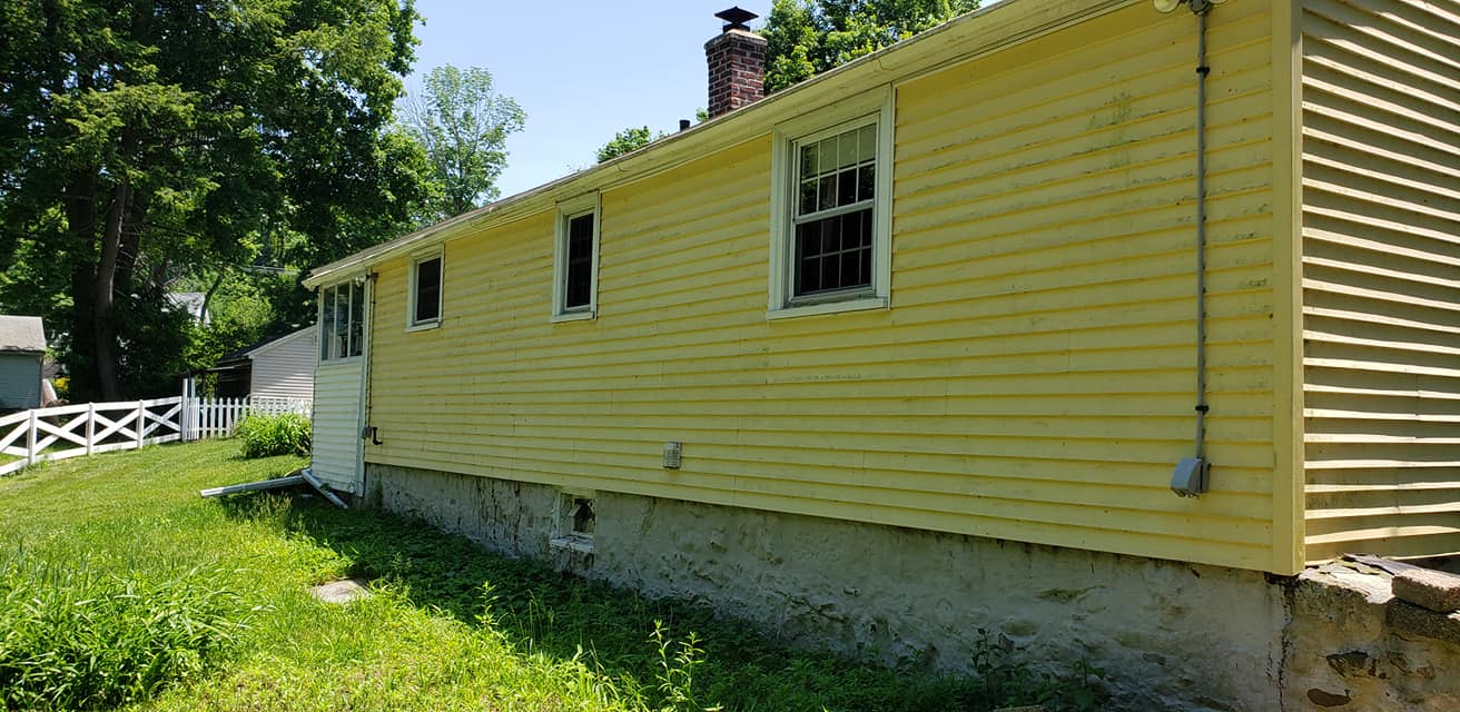 A yellow house with a lot of windows is sitting in the middle of a grassy field.