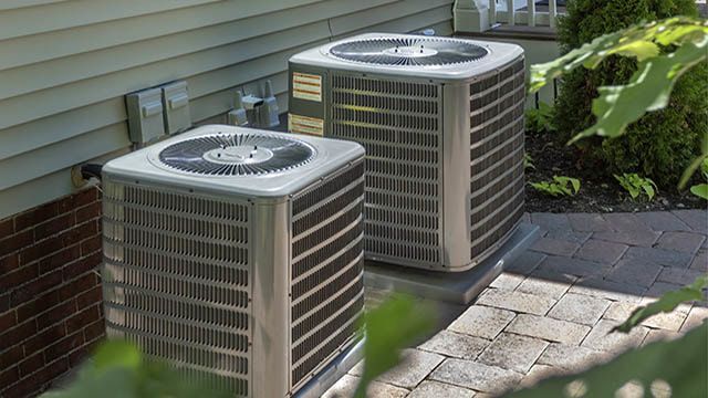 Two air conditioners are sitting on the side of a house.