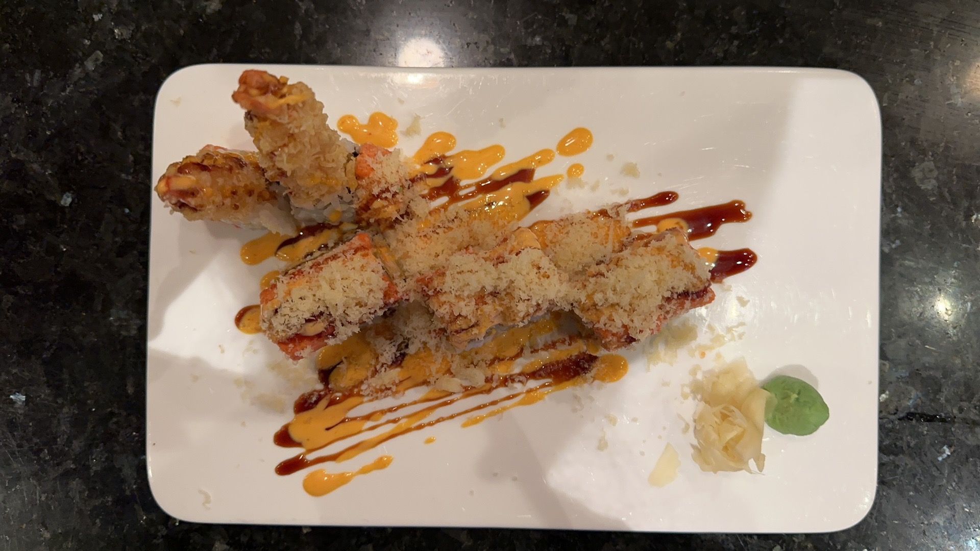 Tempura sushi roll with sauce drizzle on white plate.
