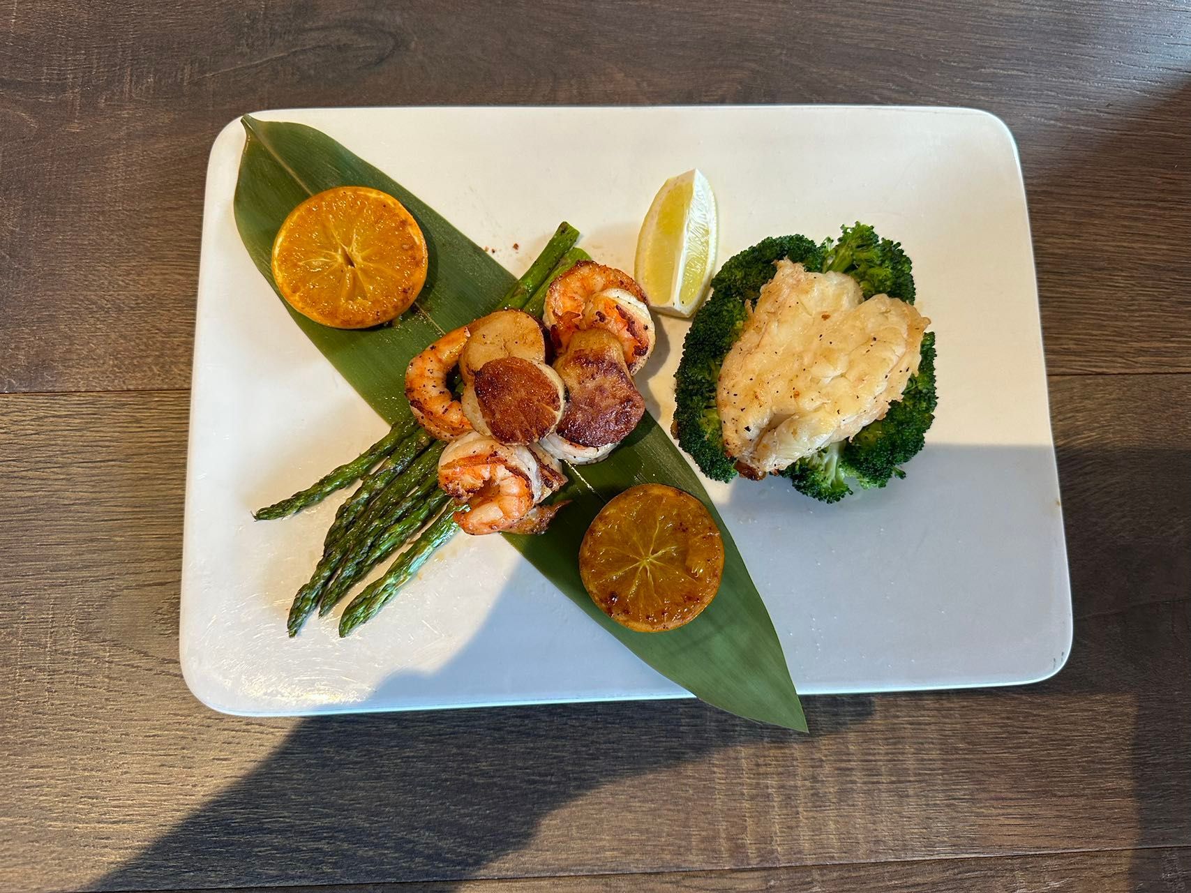 Seared scallops and shrimp with asparagus, broccoli, orange slices, and lime on a white plate.
