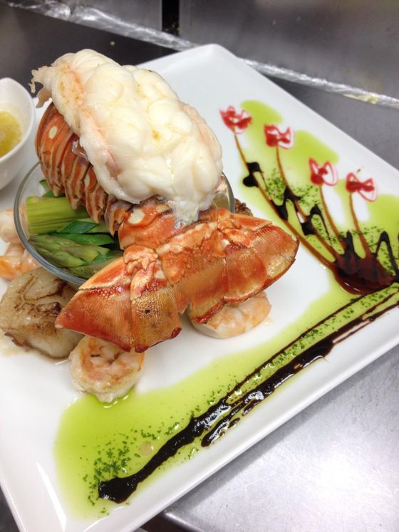 Lobster tail and claw, grilled shrimp, scallop, asparagus, artistic plate design with sauce.