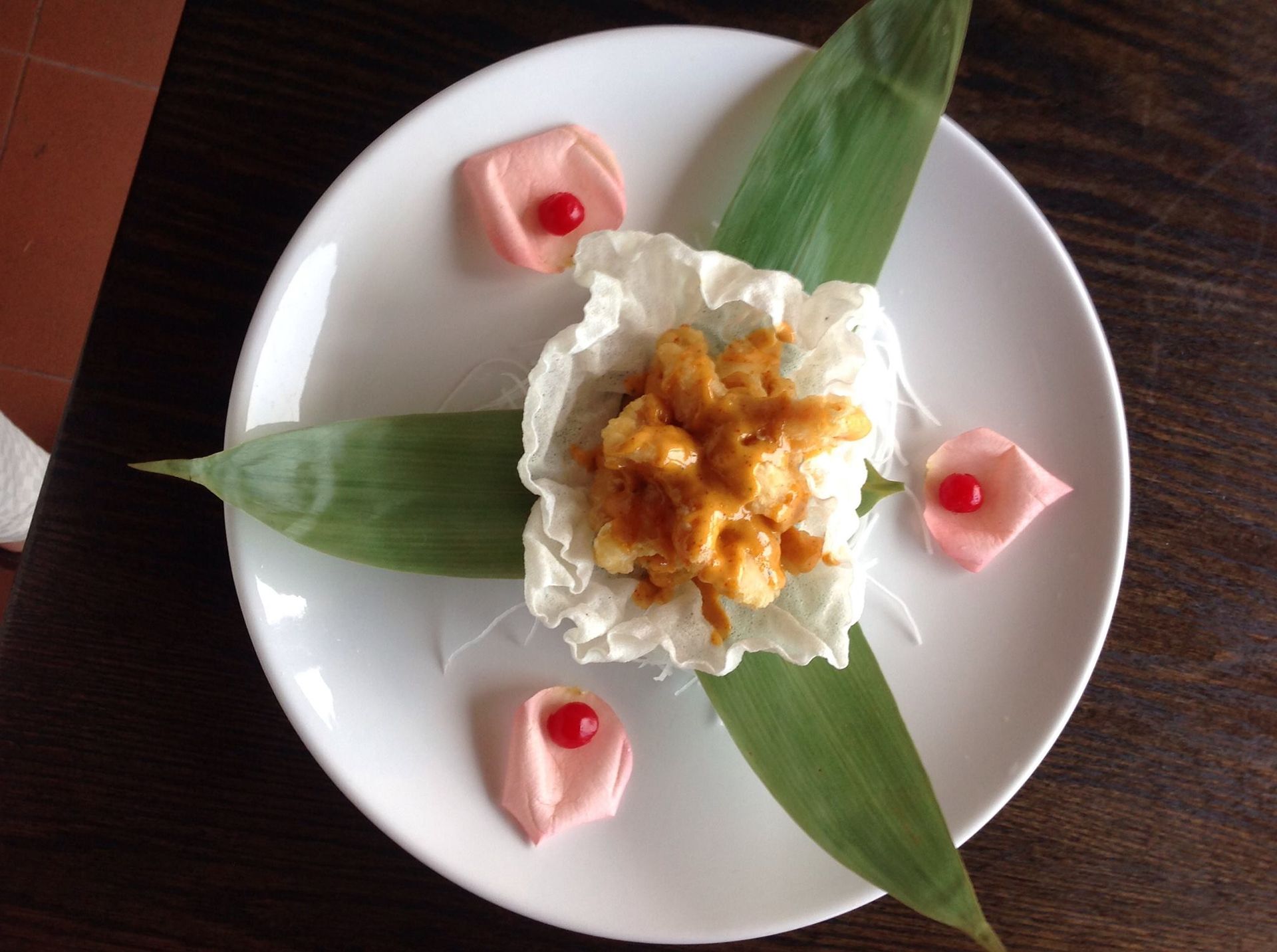 Sushi dish: fried shrimp in sauce on cabbage, with leaves and rose petals on a white plate.