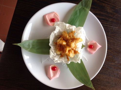 Sushi dish: fried shrimp in sauce on cabbage, with leaves and rose petals on a white plate.