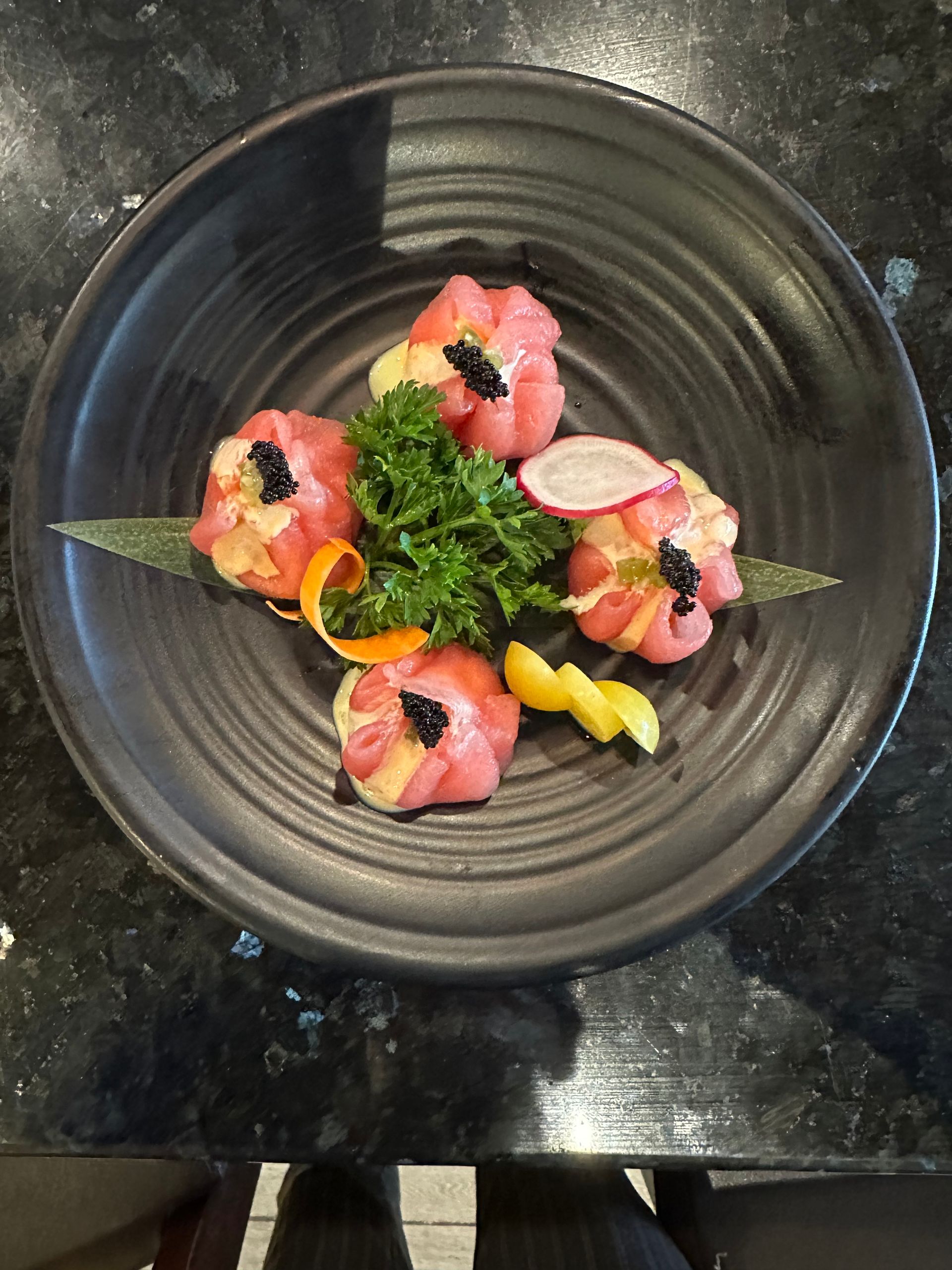 Sushi dish with pink tuna, black caviar, parsley, and radish on a black plate.
