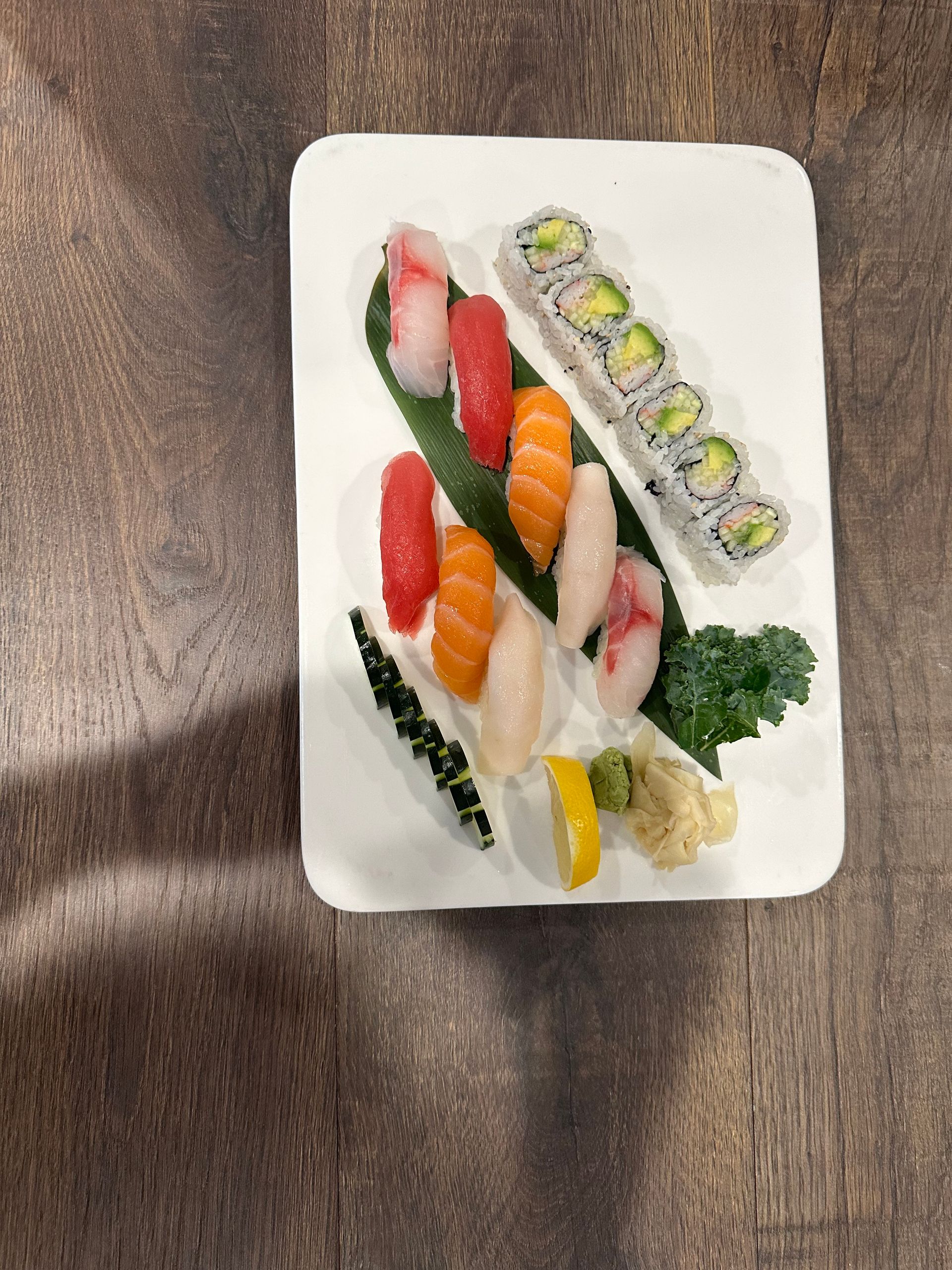 Sushi plate with nigiri, rolls, and garnishes on a wooden table.