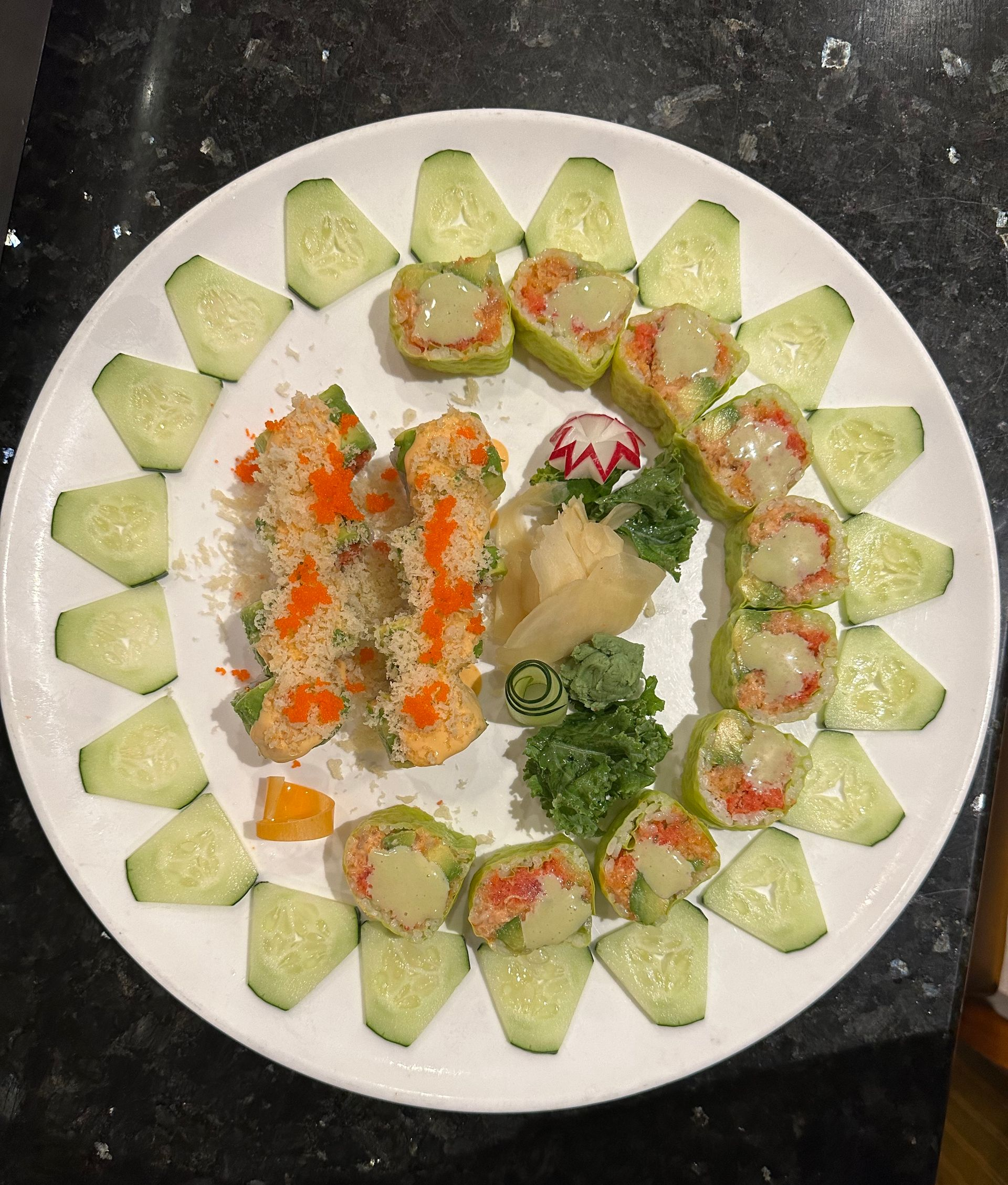 Sushi platter with rolls, cucumber slices, and garnishes on a white plate.