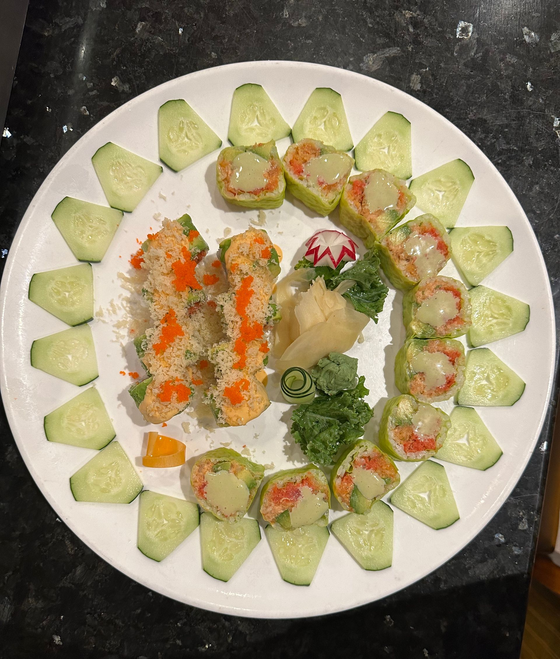 Sushi platter: rolls arranged with cucumber slices, wasabi, and pickled ginger on a white plate.