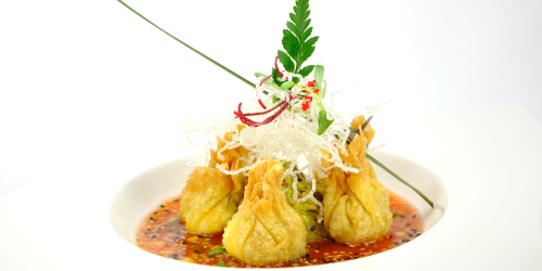 Fried dumplings in a white bowl with red sauce, topped with garnish and herbs.