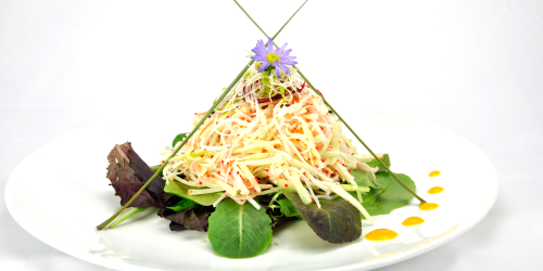 Salad on a white plate, topped with shredded vegetables and a purple flower.