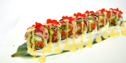 Sushi roll with various toppings and sauces on a white plate with a leaf.