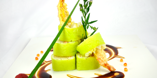 Green sushi rolls stacked on a white plate, garnished with sauce and greenery.