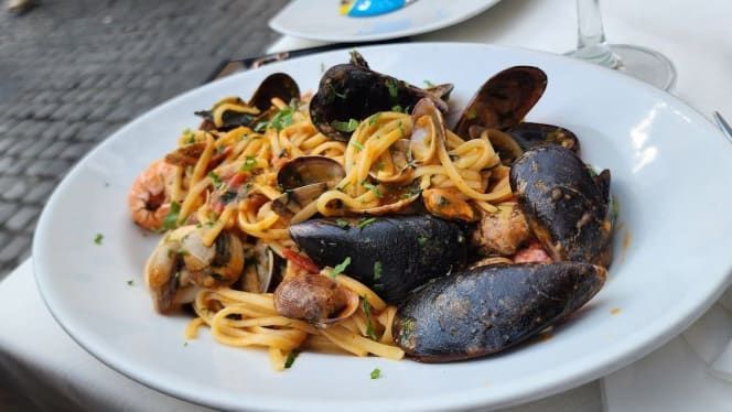 Pasta con cozze, vongole e gamberi su un piatto bianco; ristorante all'aperto.