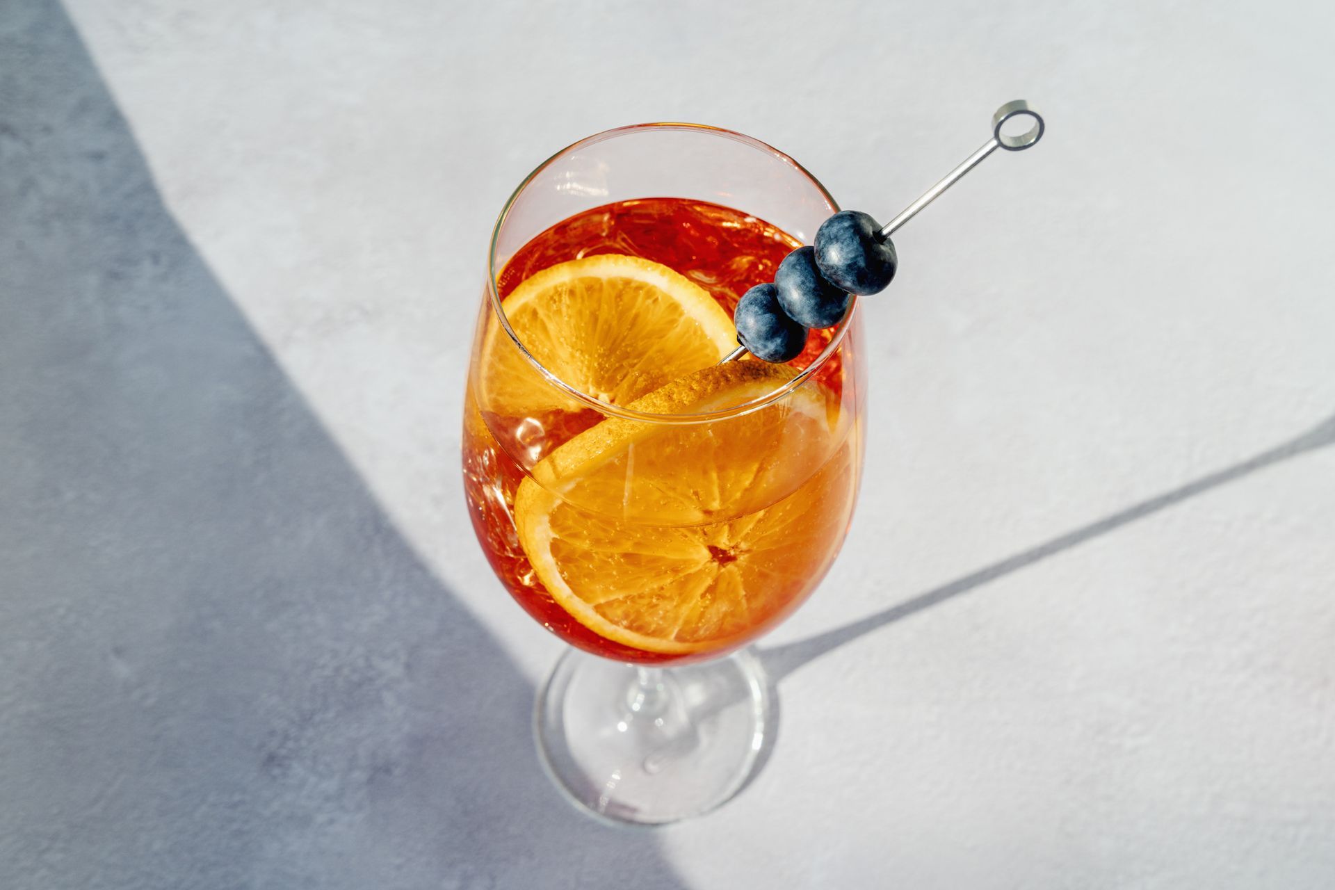Cocktail in un bicchiere con fette d'arancia e mirtilli infilzati su uno spiedino.