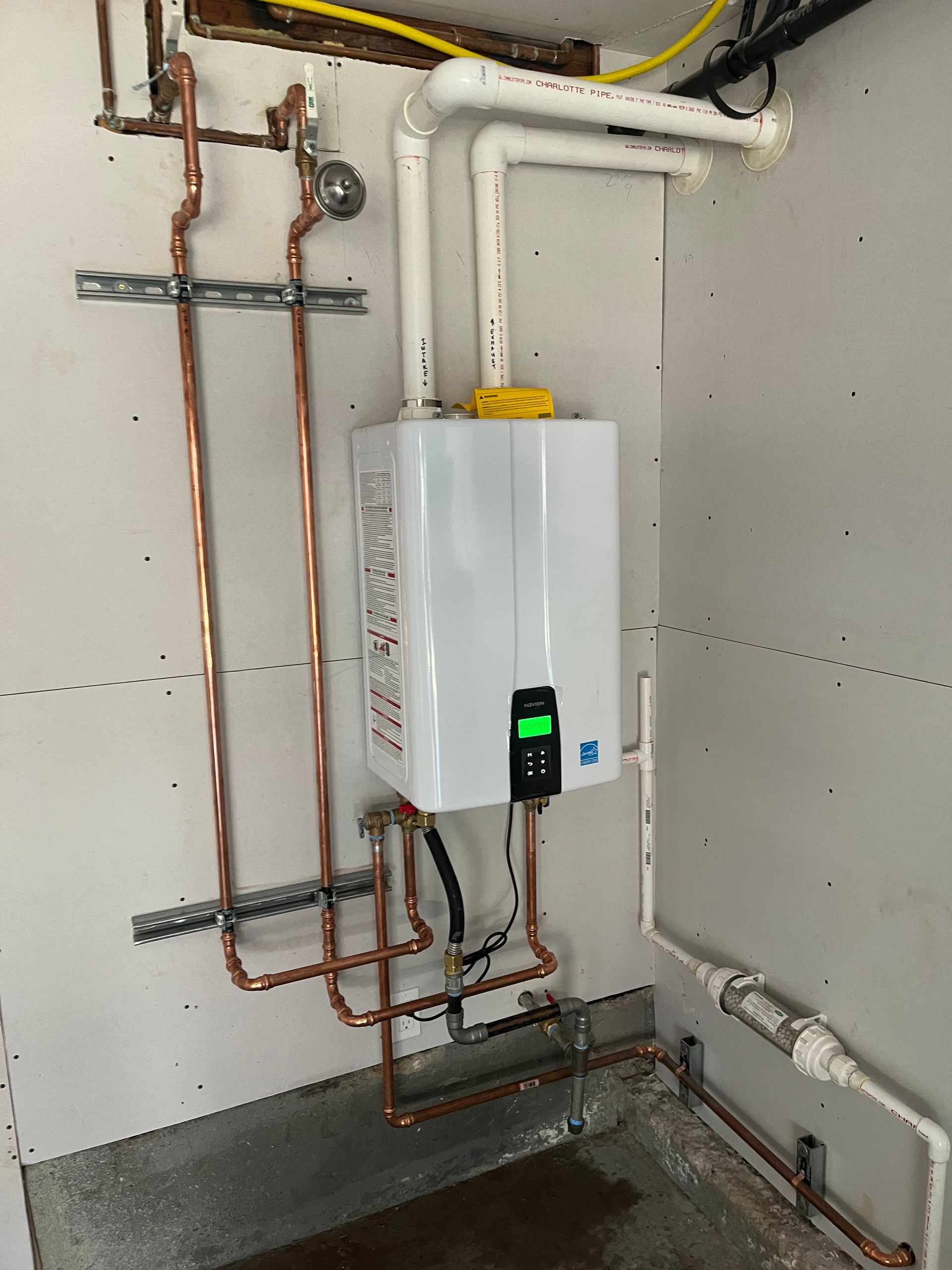 White tankless water heater with copper pipes and white PVC pipes in a utility room.