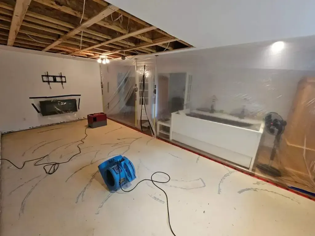 Sous-sol en rénovation avec plafond apparent, bâches en plastique et matériel de séchage.