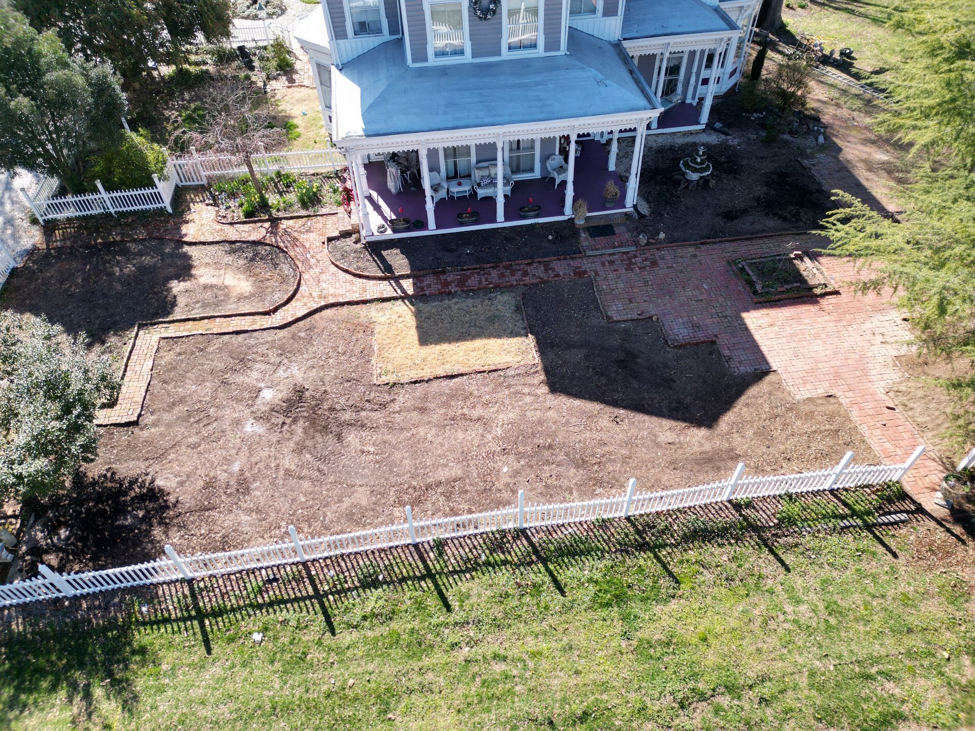 Aerial view of a Victorian house with a brick patio, picket fence, and grassy yard.