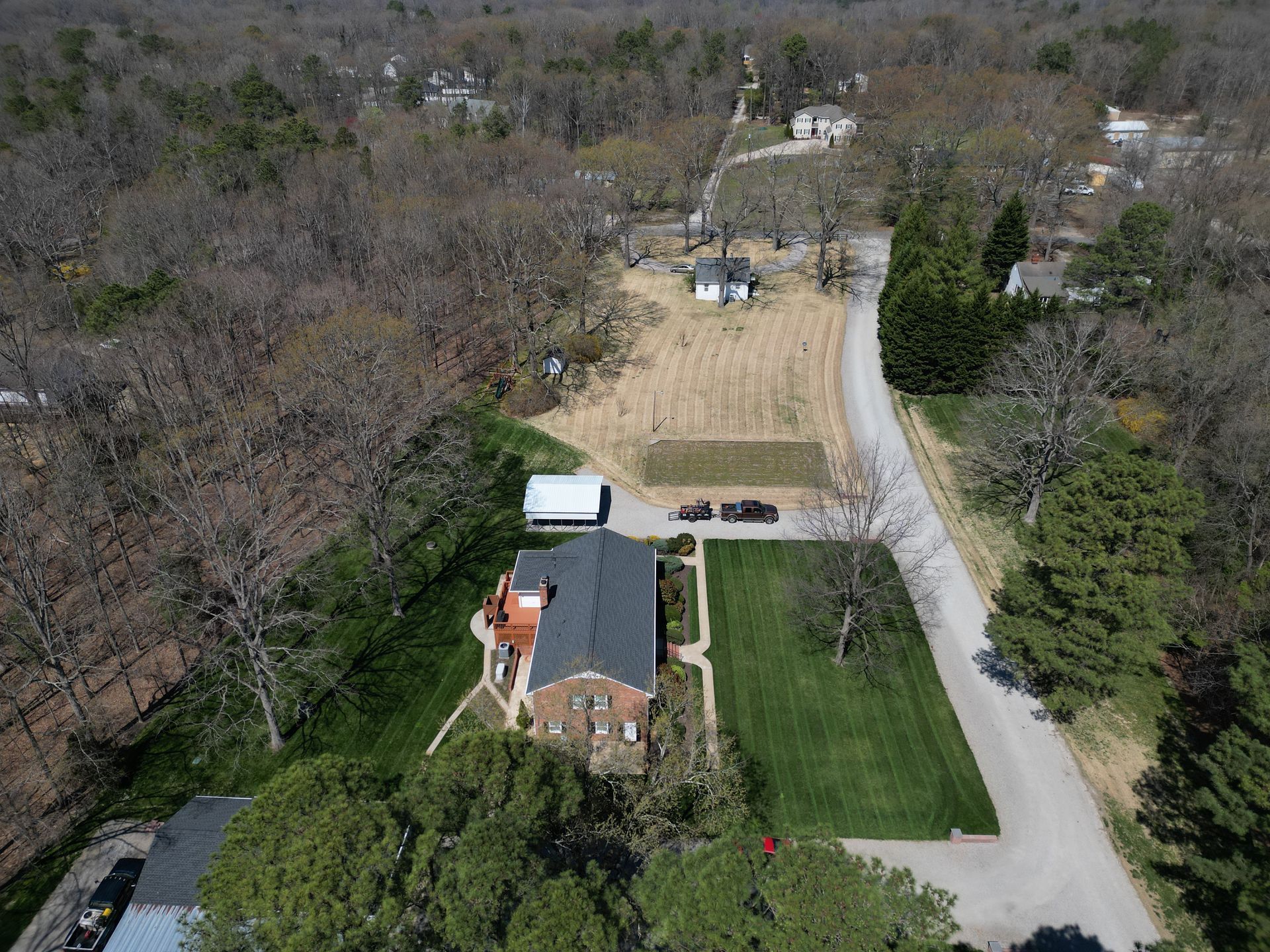 Aerial view of a house with a dark roof and a lawn, trees, and a road.