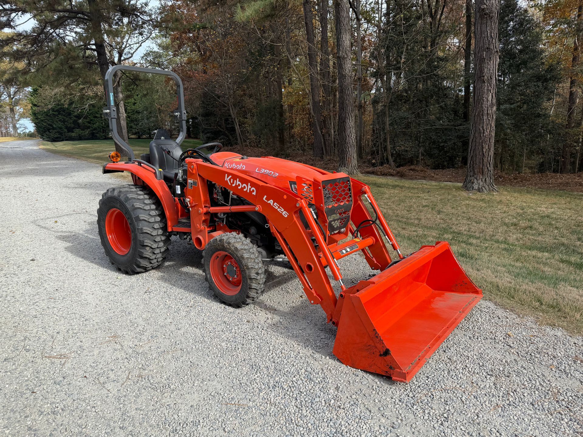 Orange Kubota tractor with a front-end loader on gravel driveway near trees.