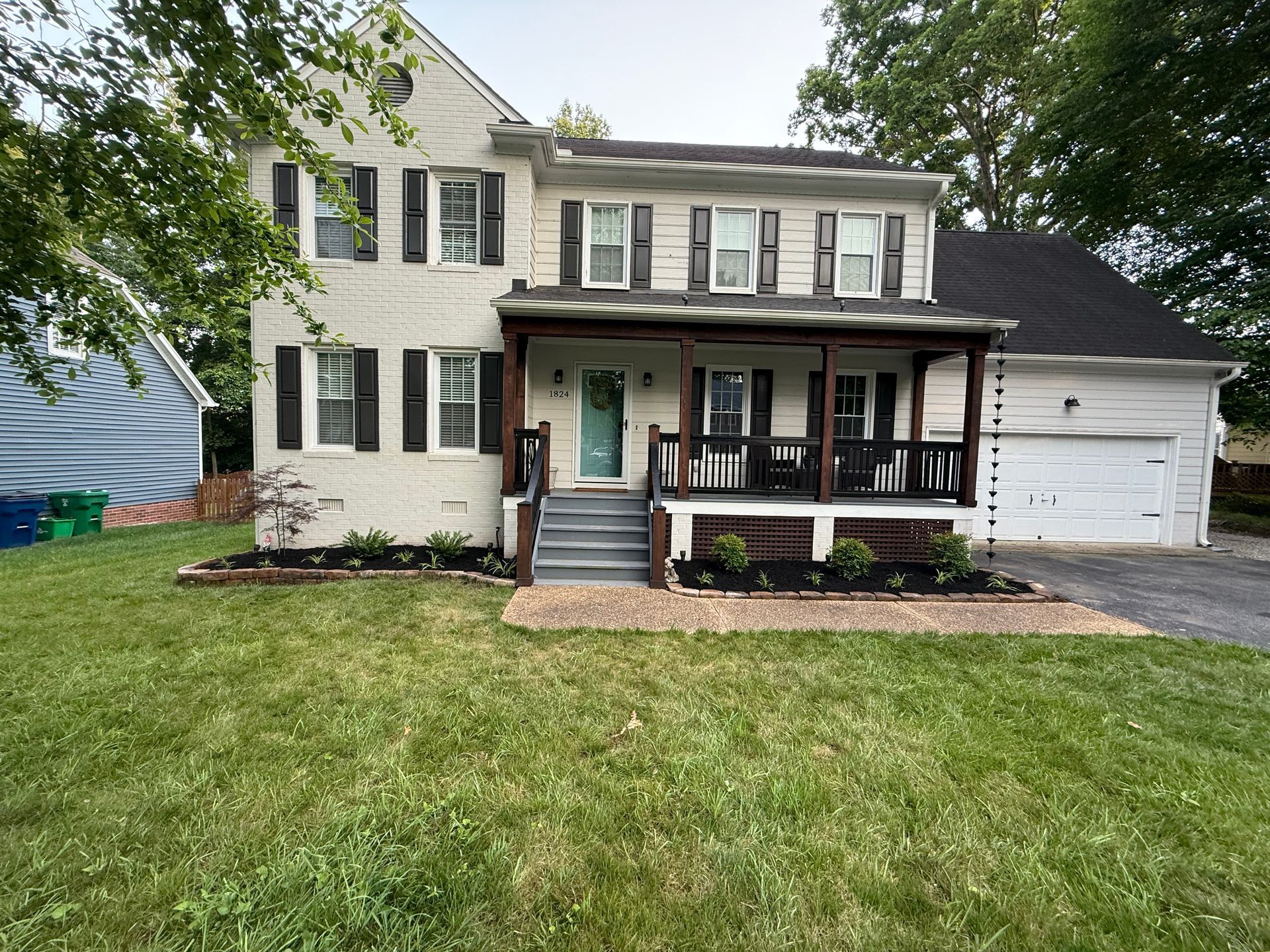 Two-story house with a porch and garage; off-white exterior with black shutters and a teal front door.