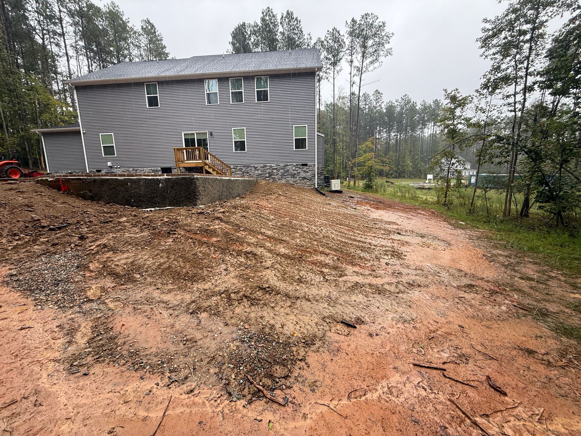 New two-story house with gray siding under construction; muddy yard, surrounding trees.