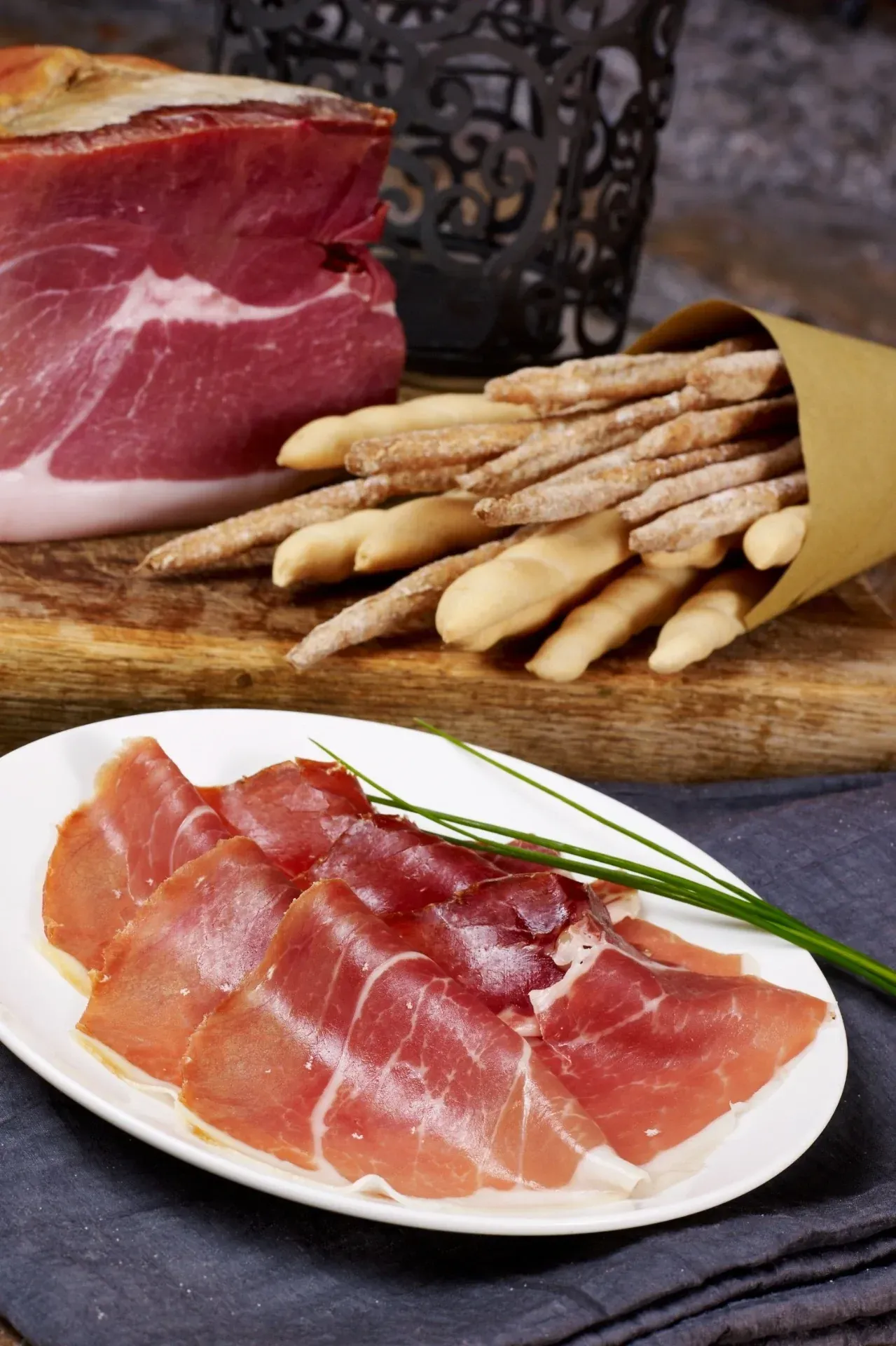 Un piatto di prosciutto crduo dolde d'osvaldo con grissini su un tavolo.