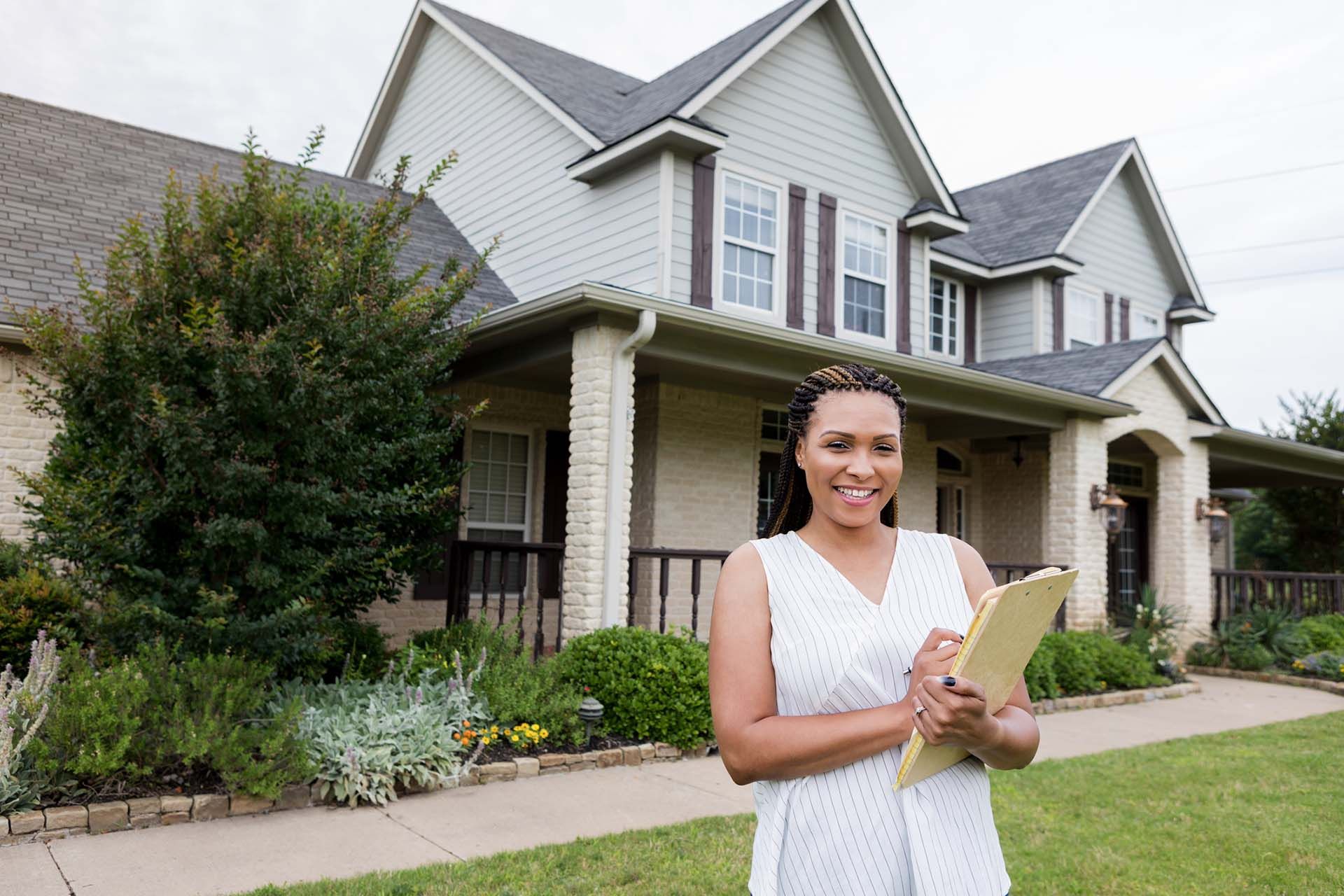 A woman is standing in front of a house holding a clipboard