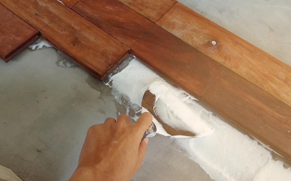 A Person Is Applying White Paint to A Wooden Floor with A Spatula — John Chisholm Flooring in Port Douglas,  QLD