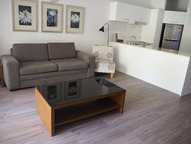 A Living Room With a Couch, Chair, Coffee Table and Kitchen — John Chisholm Flooring in Manunda,  QLD