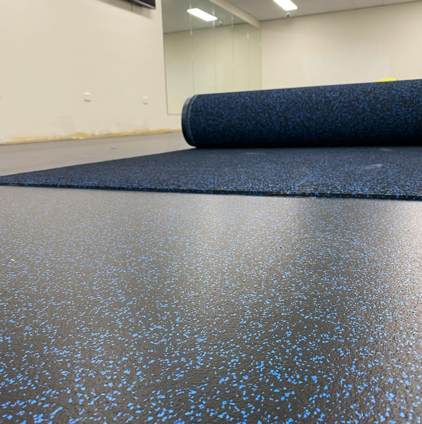 A Roll of Blue Rubber Flooring is Sitting on Top of a Black Floor — John Chisholm Flooring in Mission Beach, QLD