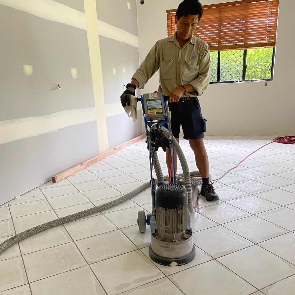 A Man is Grinding a Tile Floor With a Machine — John Chisholm Flooring in Manunda,  QLD