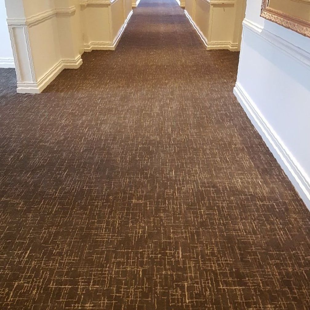 A Long Hallway With a Brown Carpet and White Walls — John Chisholm Flooring in Manunda,  QLD