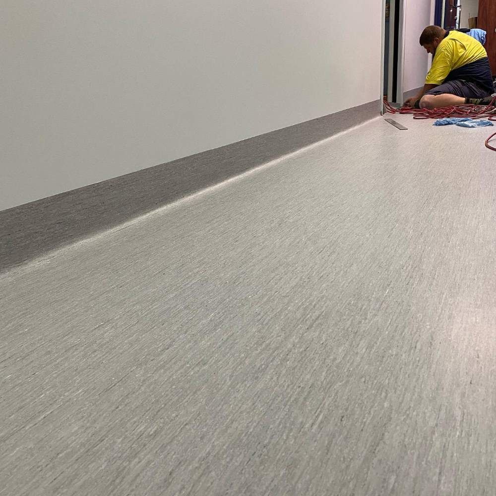 A Man is Kneeling on the Floor in a Hallway — John Chisholm Flooring in Manunda, QLD