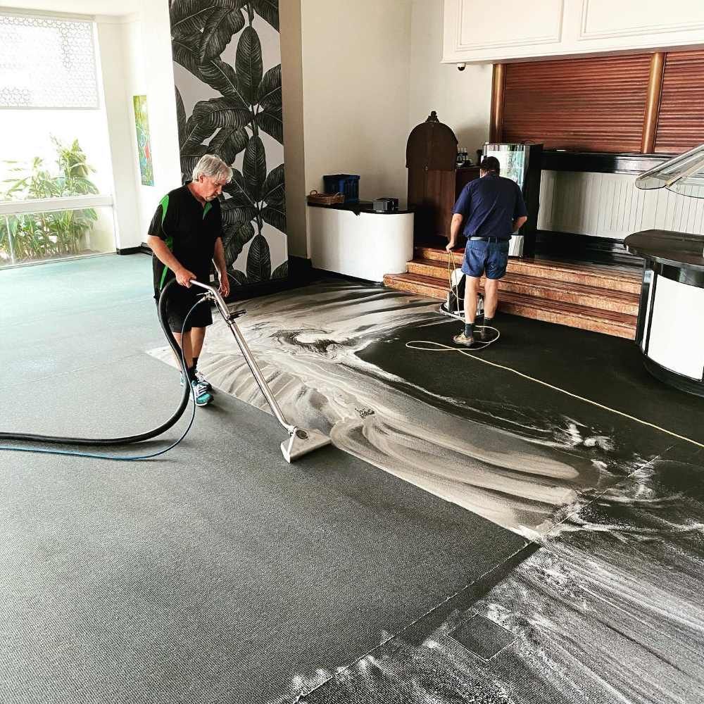 A Man is Cleaning a Carpet With a Vacuum Cleaner in a Room — John Chisholm Flooring in Manunda, QLD