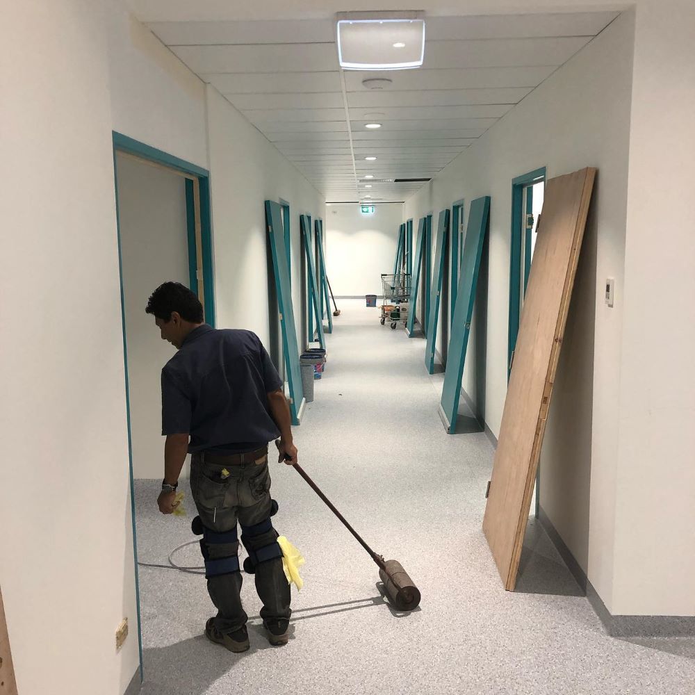 A Man is Cleaning a Hallway With a Vacuum Cleaner — John Chisholm Flooring in Manunda, QLD