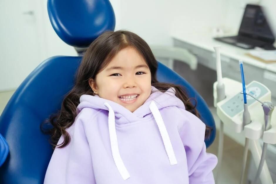 A little girl is sitting in a dental chair and smiling.