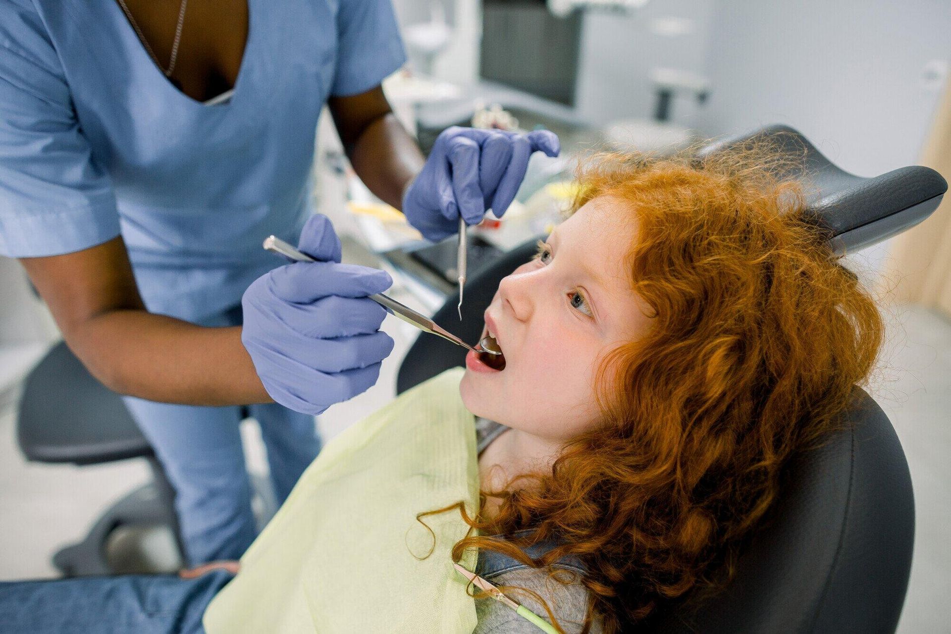 A young girl is sitting in a dental chair getting her teeth examined by a dentist.