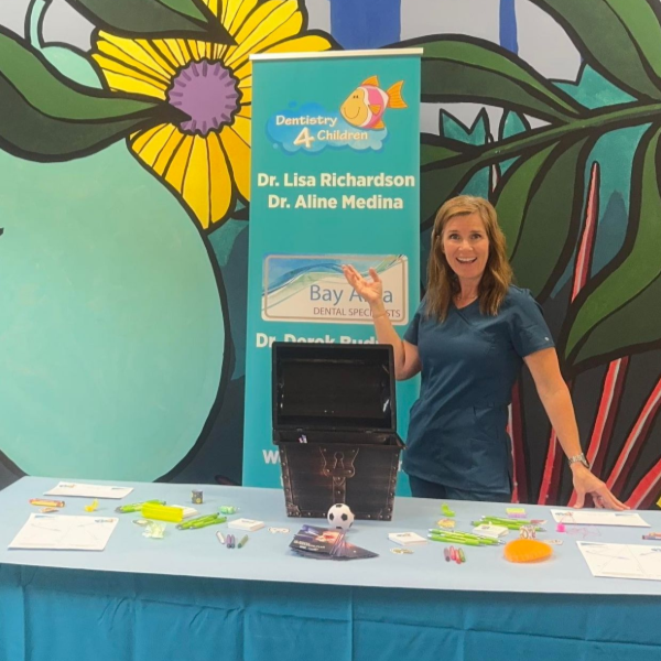 A person stands at a table with a display banner in front of a colorful, large-scale botanical mural.