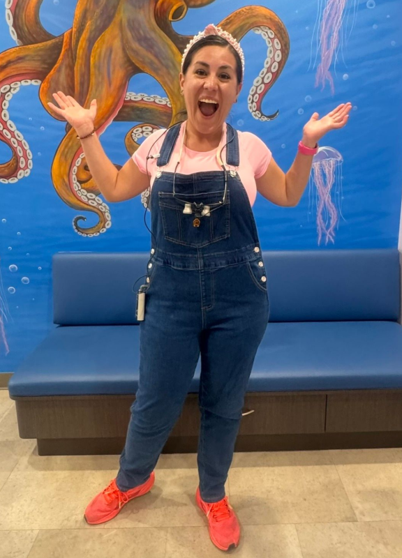 Woman in denim overalls and red shoes posing excitedly in front of an octopus mural and blue bench