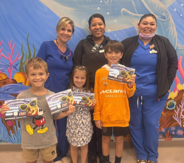 Three adults and three children stand together smiling in front of a colorful underwater-themed mural.