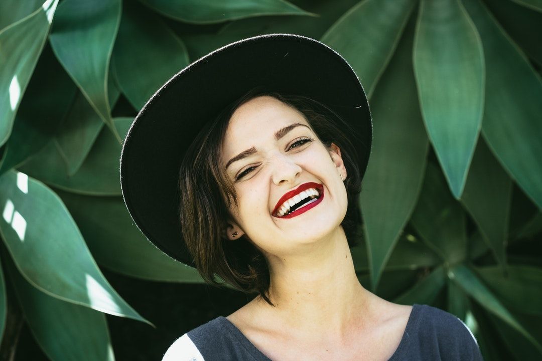 a woman wearing a black hat and red lipstick is smiling