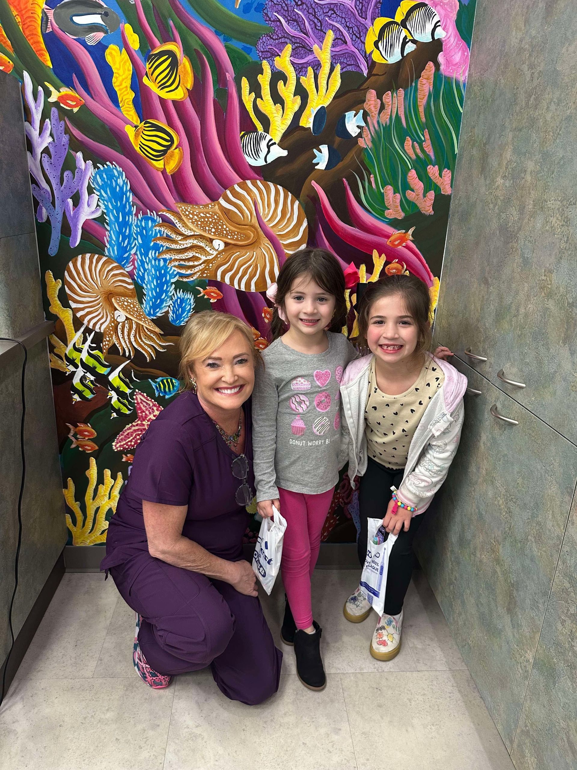 A woman is kneeling down next to two little girls in front of a mural.